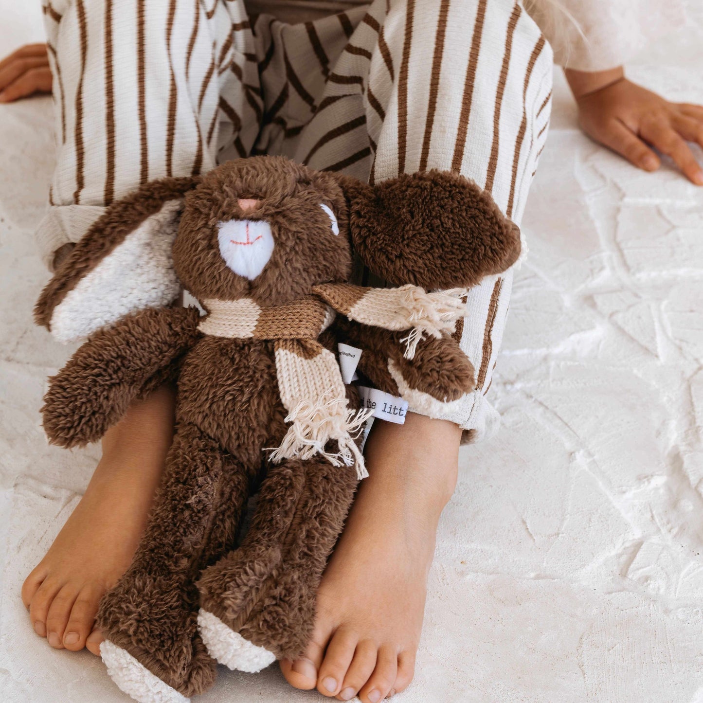 Frankie Sr. the Bunny plush toy with soft brown fur and striped scarf next to child's feet