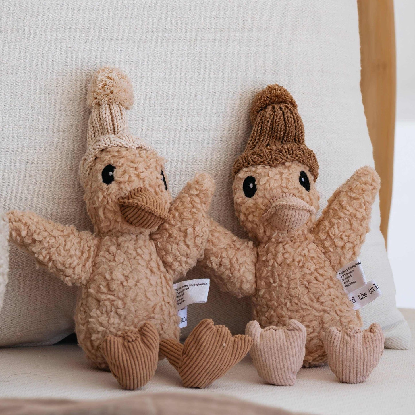 Two plush Edmond the Duck toys with knitted hats sitting on a couch