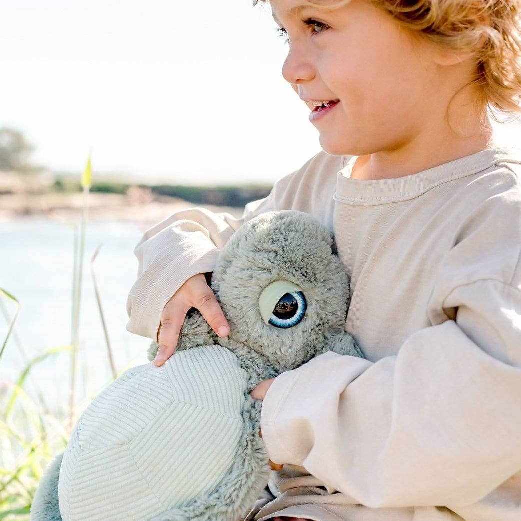 Child holding soft plush turtle toy Tyler the Turtle outdoors near water