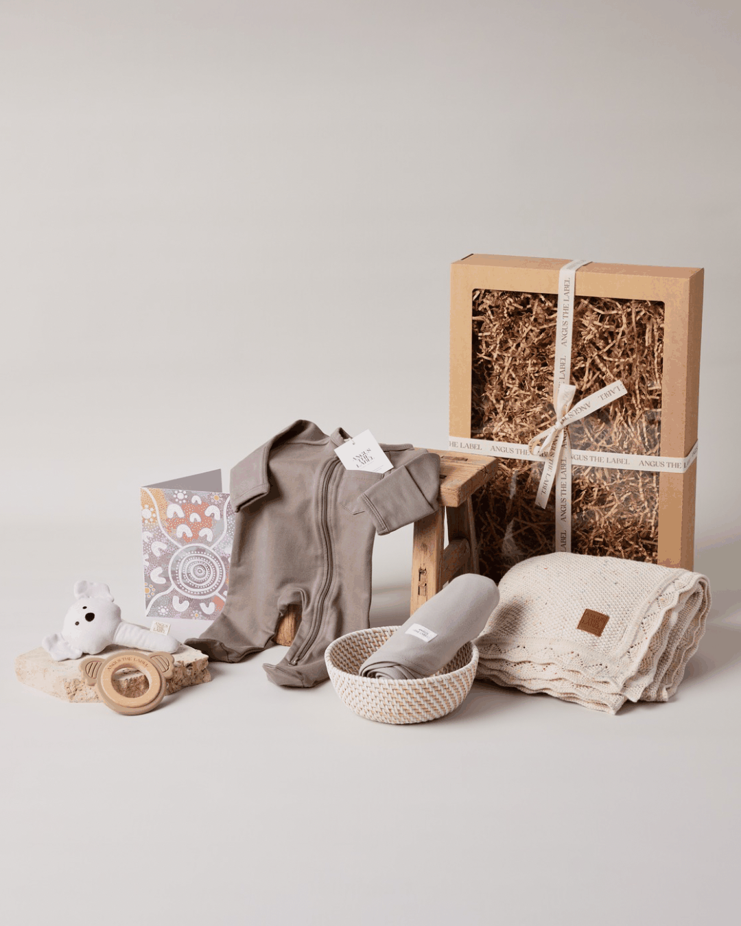 Cuddle & Care Baby Gift Set with cotton blanket, mocha onesie, swaddle wrap, teething ring, plush bunny rattle, and gift card in a gift box