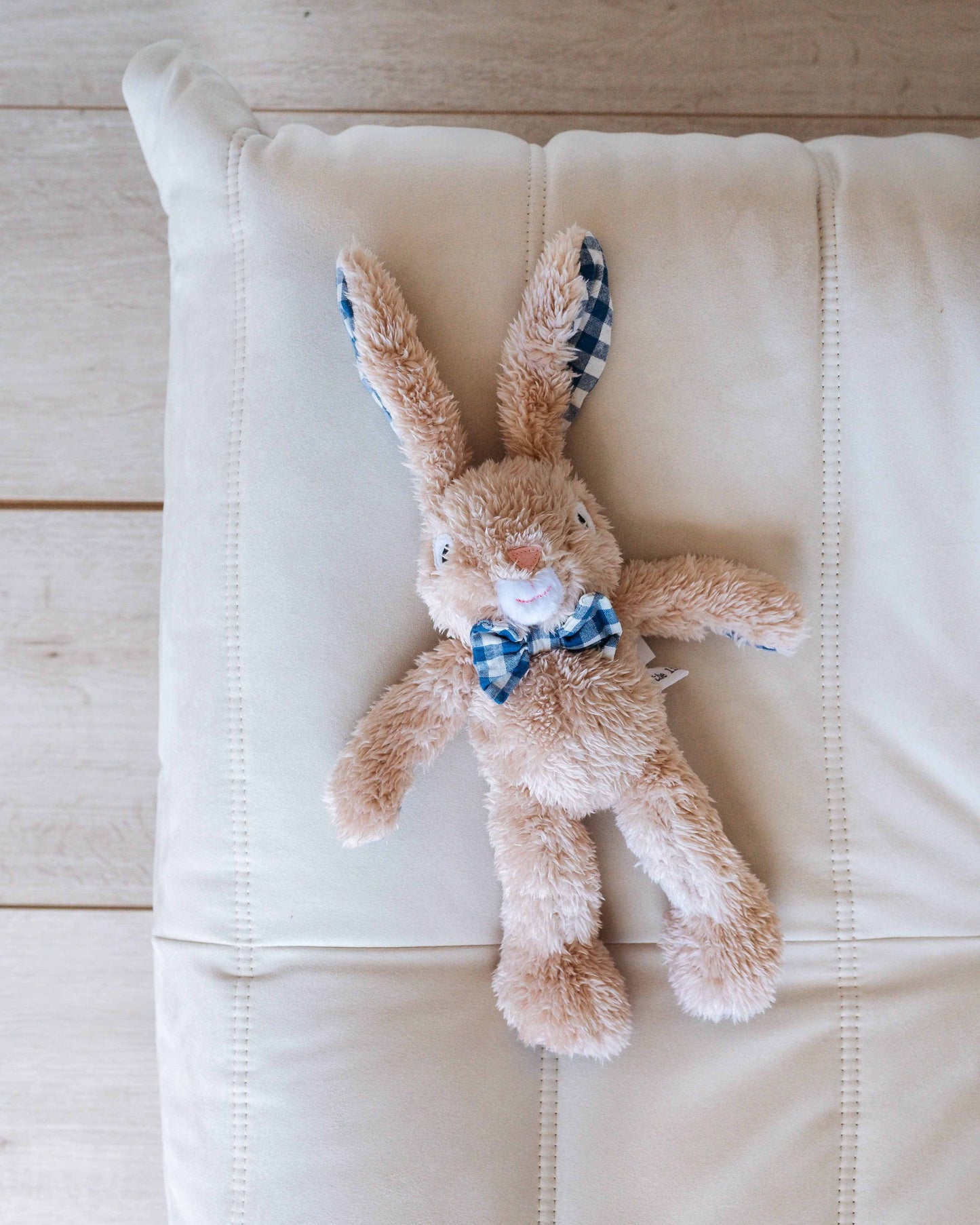 Louis Sr. the Bunny plush with caramel soft fabric and blue gingham bow tie on white cushion