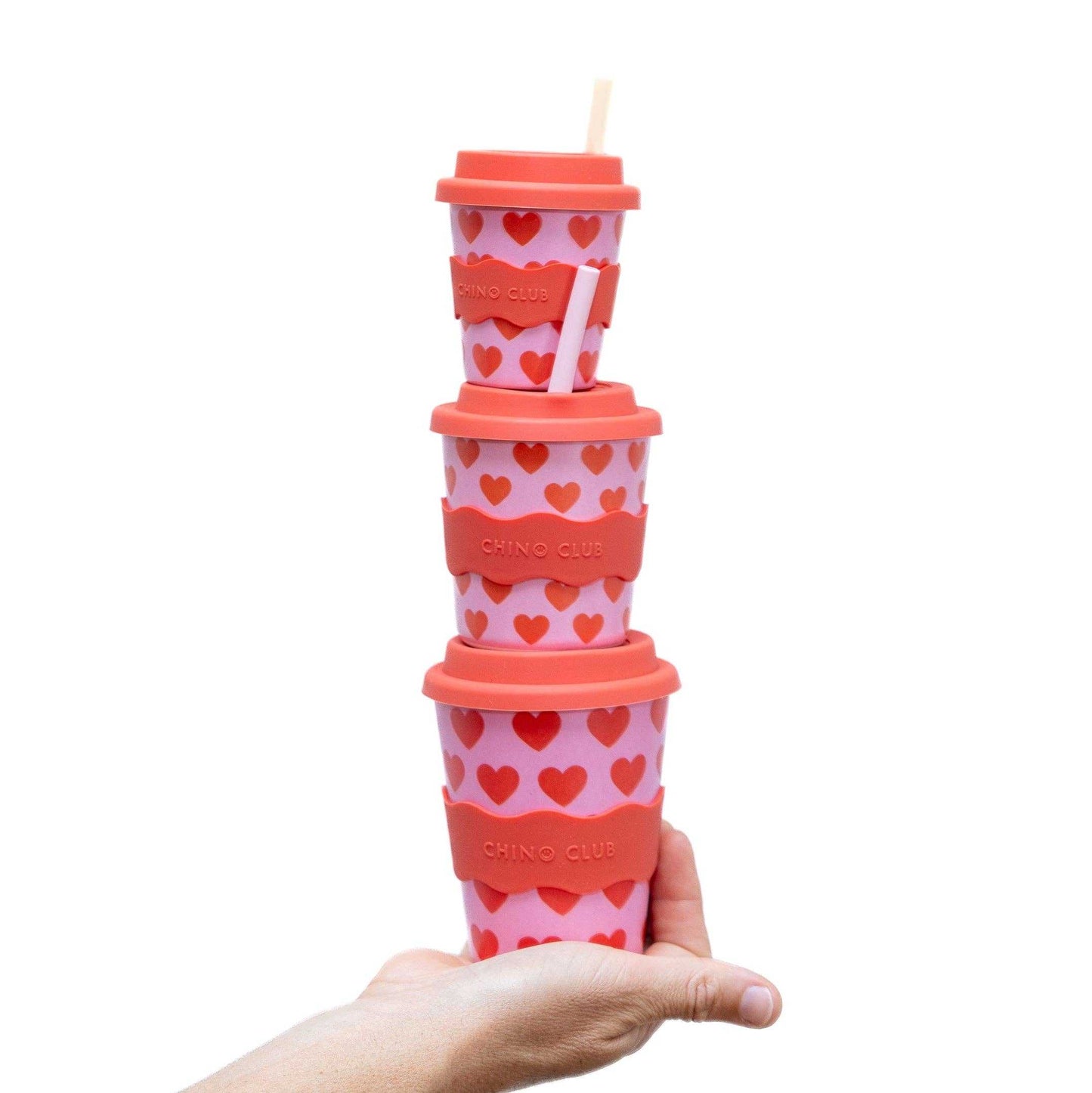 Stack of pink Hearts Babychino Cups with red heart patterns and lids held in hand