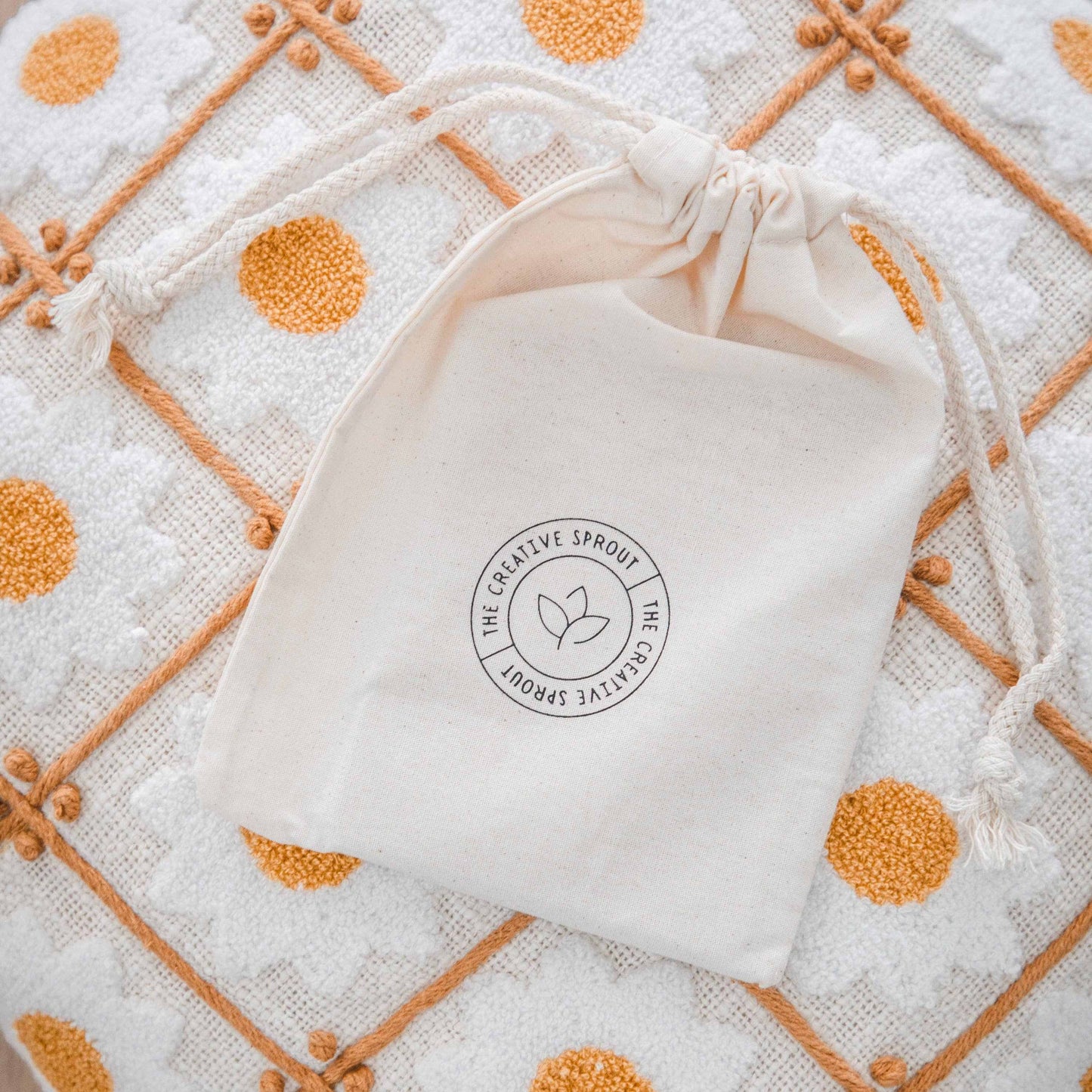 Drawstring pouch with The Creative Sprout logo on textured orange and white patterned fabric background for storing magnetic daily routines cards.