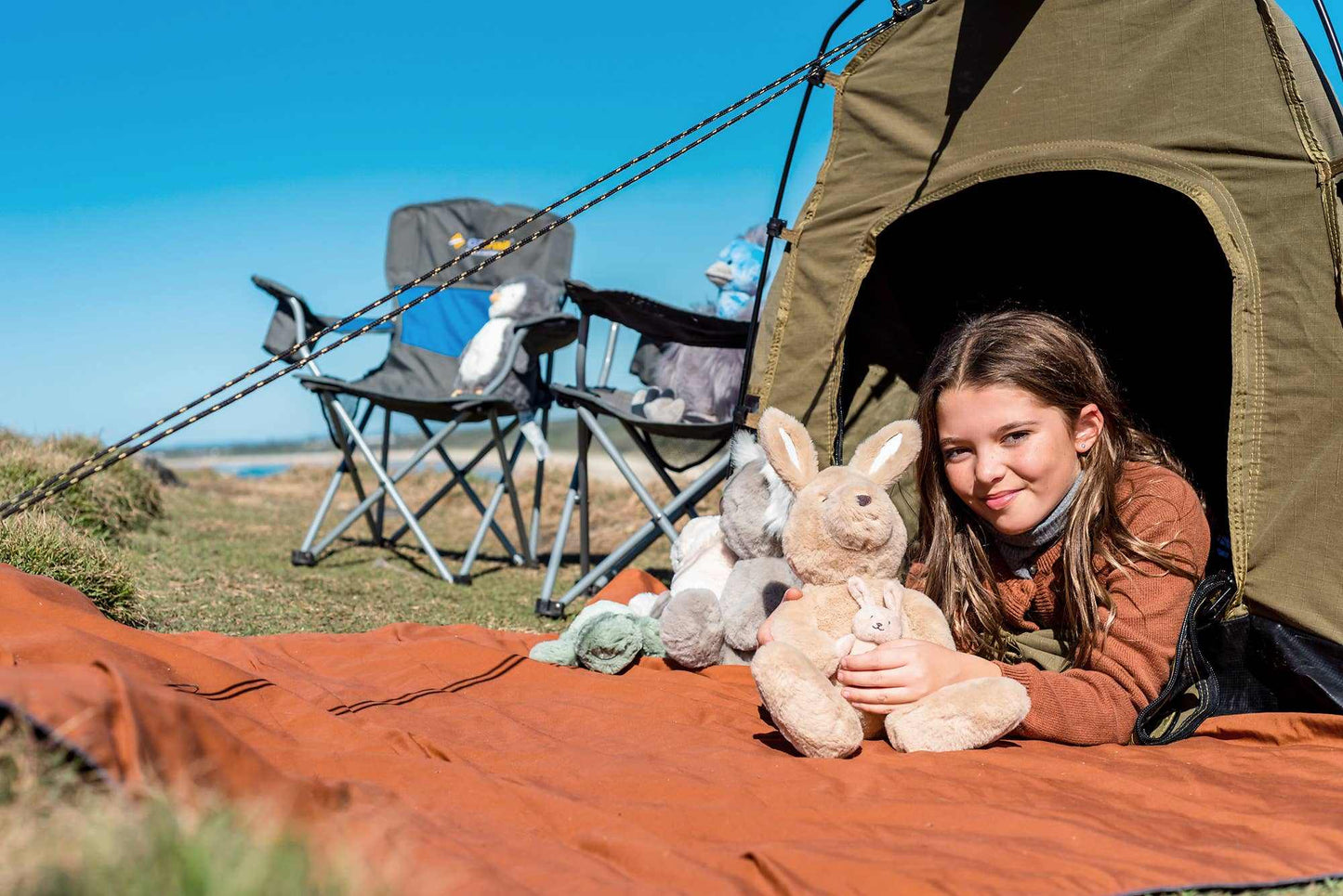 Child holding Kip & Joey kangaroo soft toy outside a tent on a camping trip