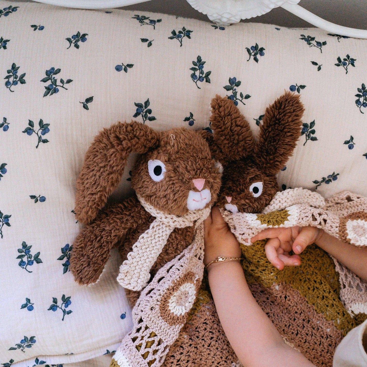 Frankie Jr. the Bunny soft plush toy cuddled by child with scarf on floral bedding