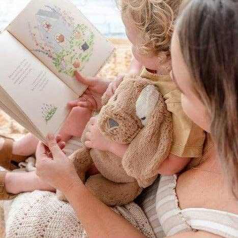 Child cuddling Duke the Dog Soft Toy while reading a book with an adult