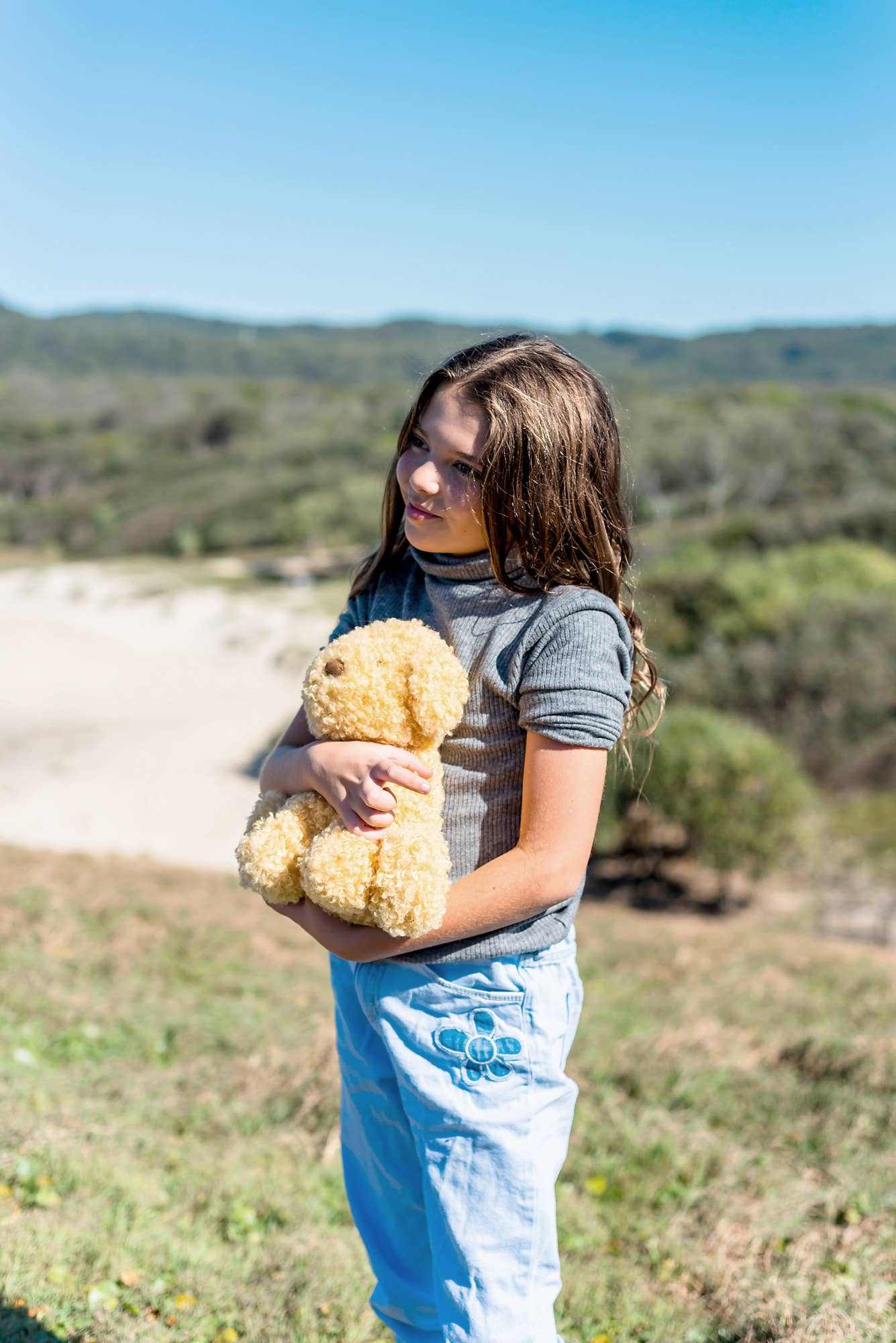Child holding Luca the Labradoodle soft toy outdoors in a sunny landscape