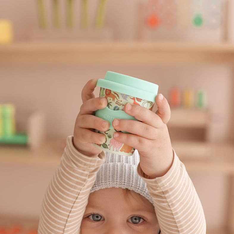 Baby holding eco-friendly Safari Babychino Cup with animal prints and teal lid
