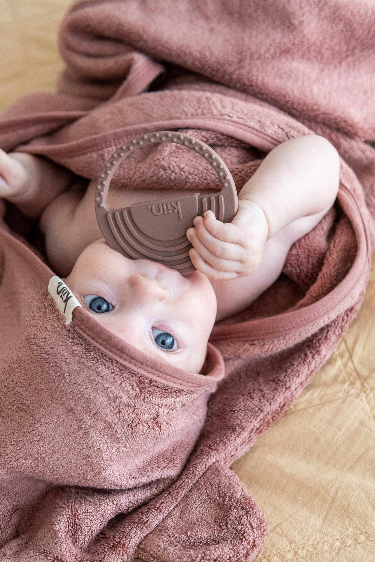 Baby wrapped in Kiin Hooded Towel with bear ears holding a teether