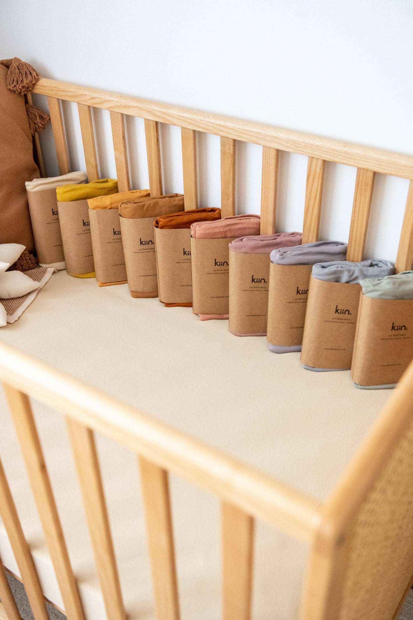 A selection of fitted cot sheets in various colors neatly placed along a wooden cot rail.