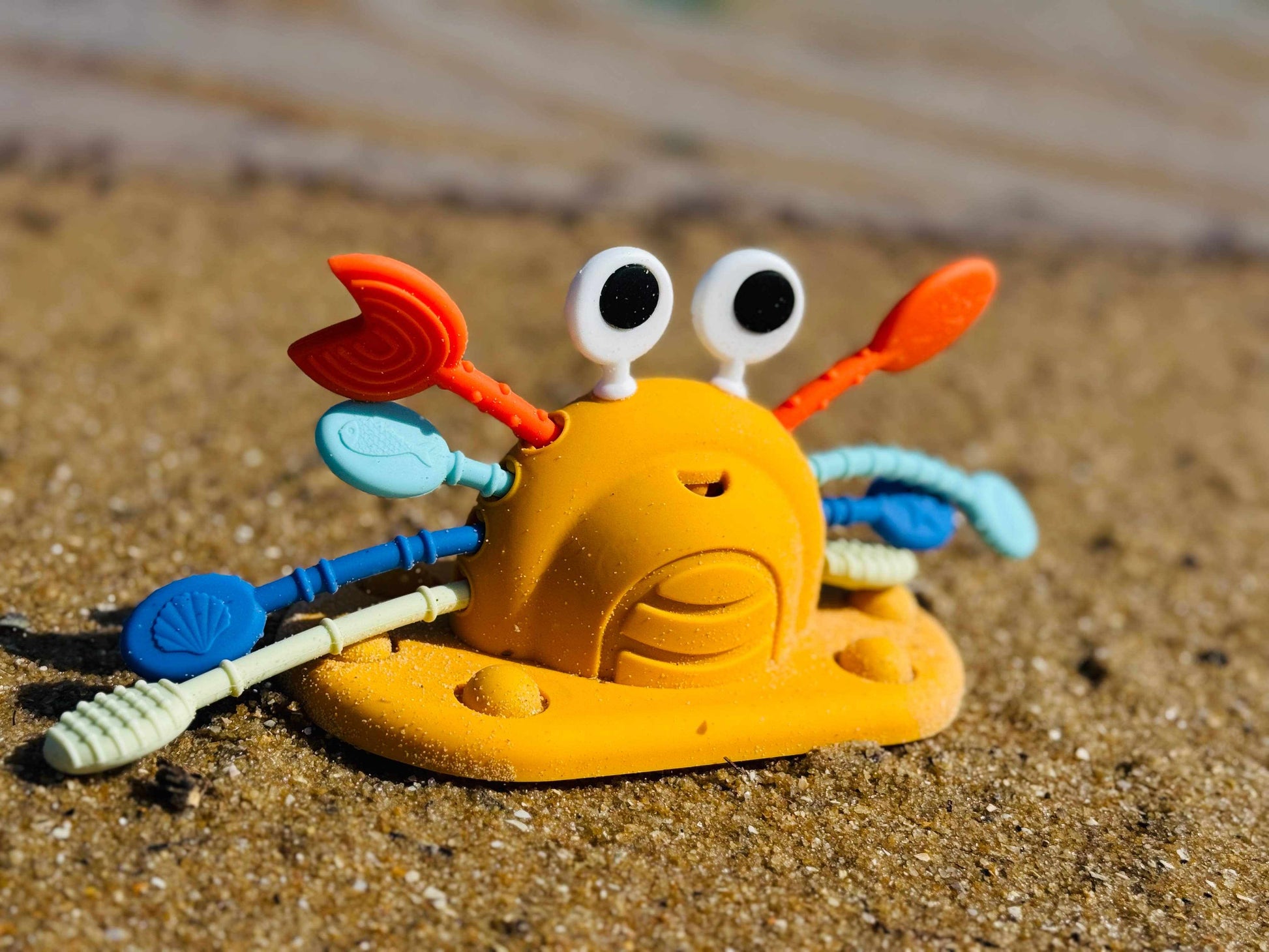 Silicone crab pull string sensory toy for toddlers with colorful pull strings on sandy surface