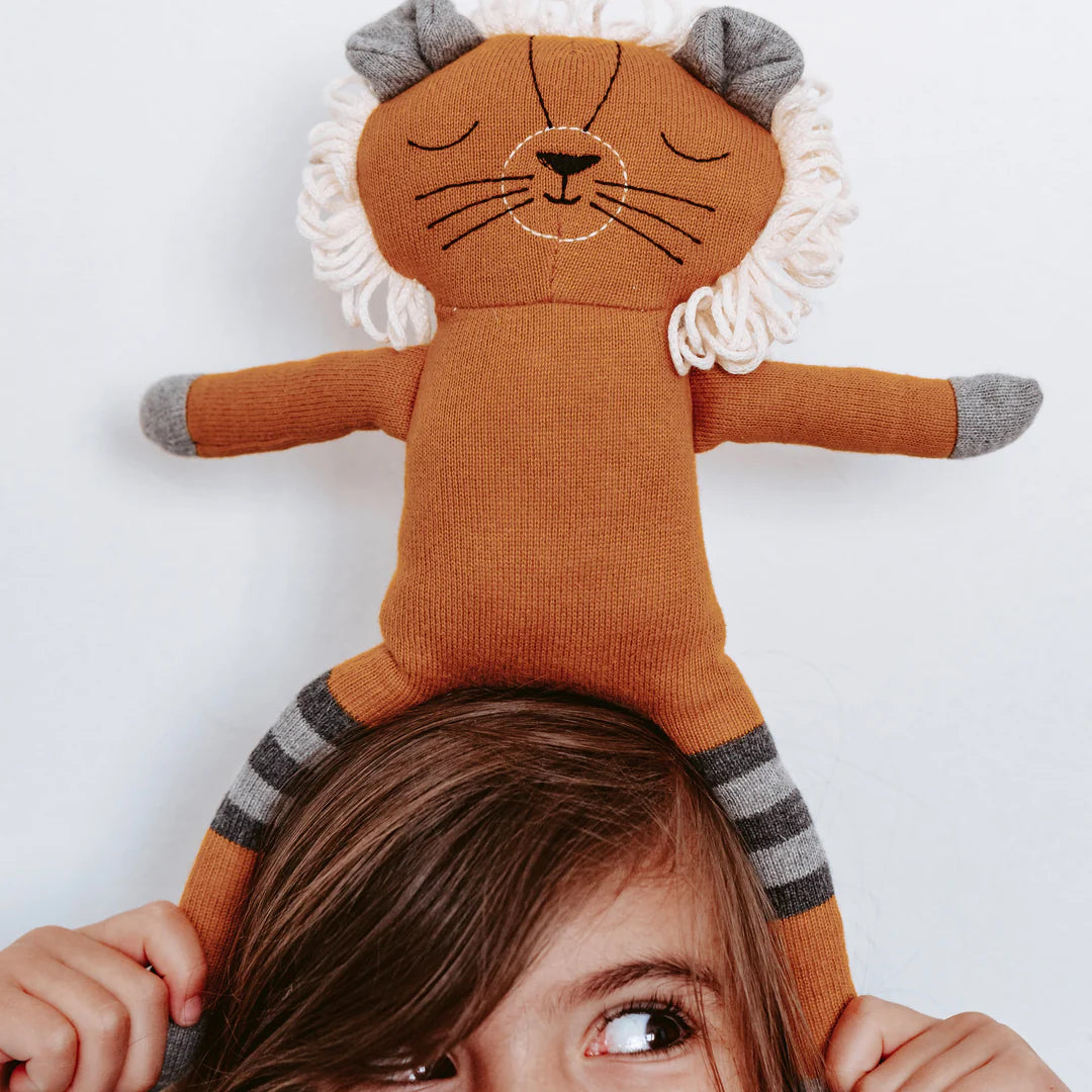 Child holding a lion-shaped plush toy on their head against a white background