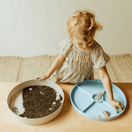 Toddler playing with Sensory Kits Galaxy featuring black rice, stars, and space-themed items on divided tray