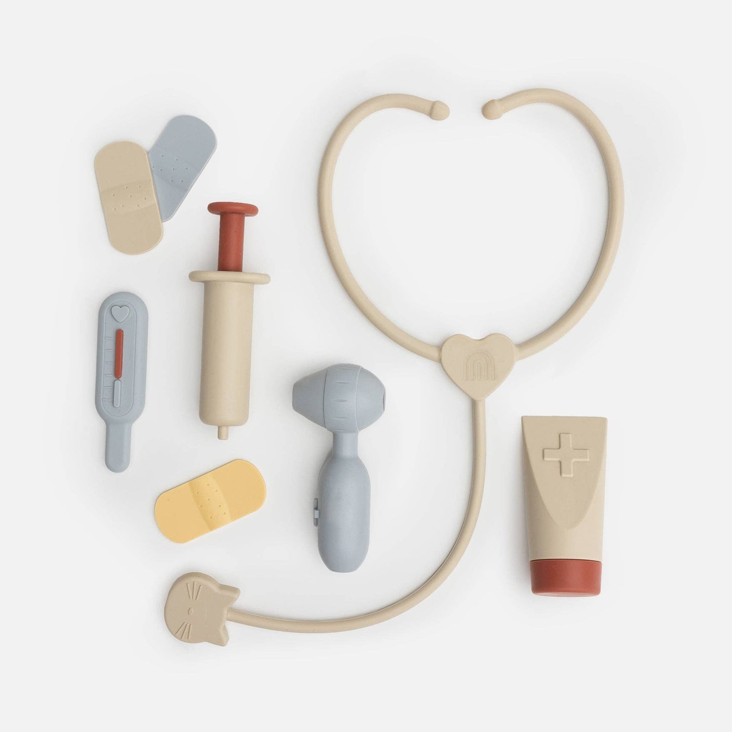 A collection of Kynd silicone medical playset items including a stethoscope, syringe, and other tools laid out on a white background.