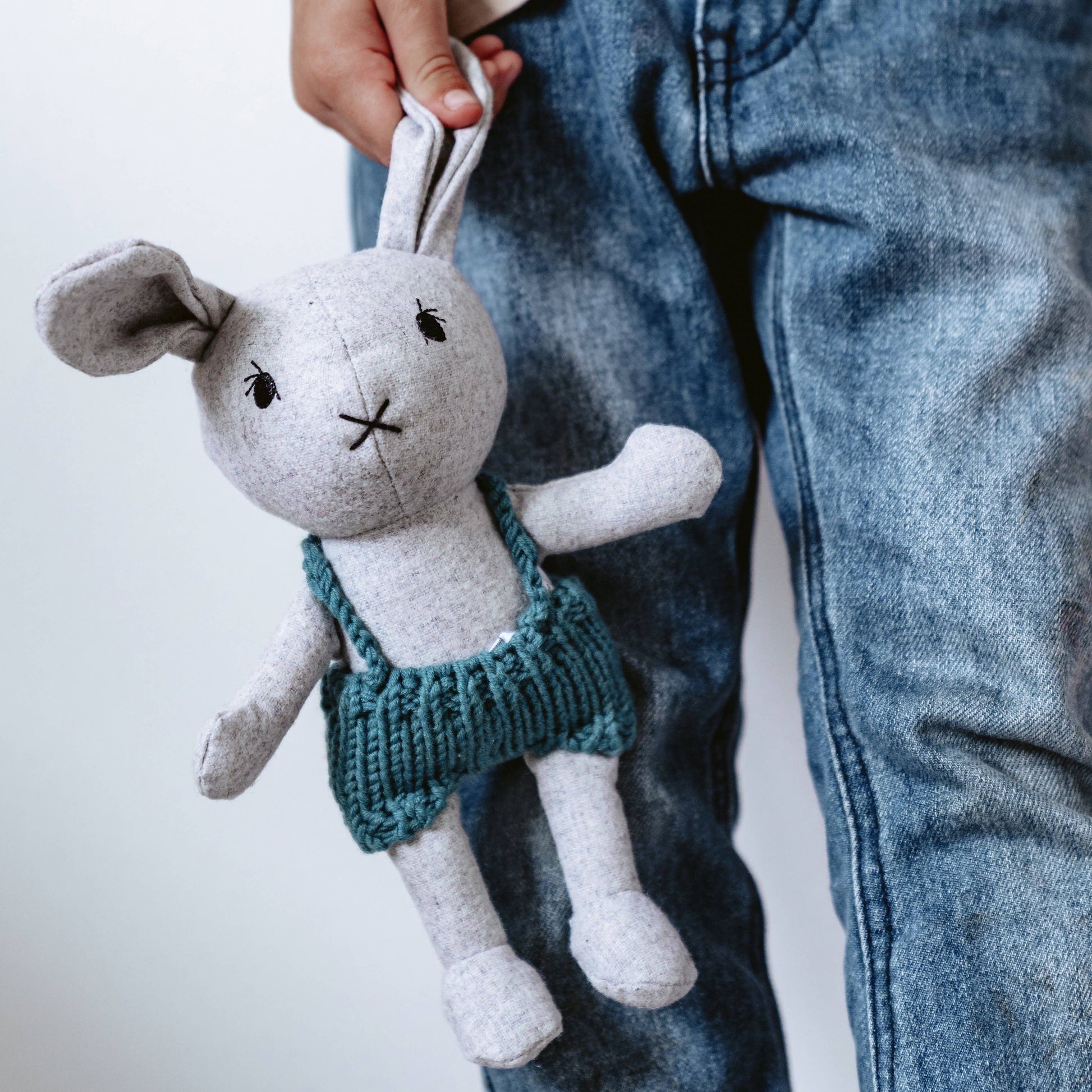 A plush toy resembling a bunny with large floppy ears and a teal-colored dress, being held by a person wearing blue jeans.
