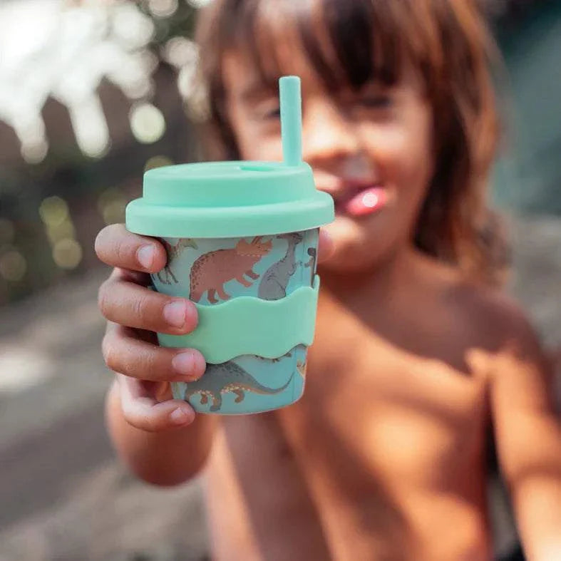 Child holding eco-friendly Dino Babychino Cup with silicone lid and dinosaur design, 4oz capacity
